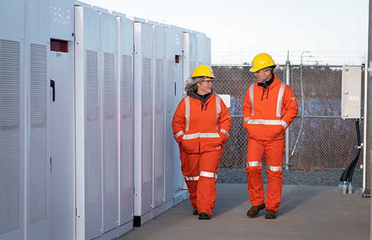 Two utility workers in hard hats and safety coveralls discussing a project site.